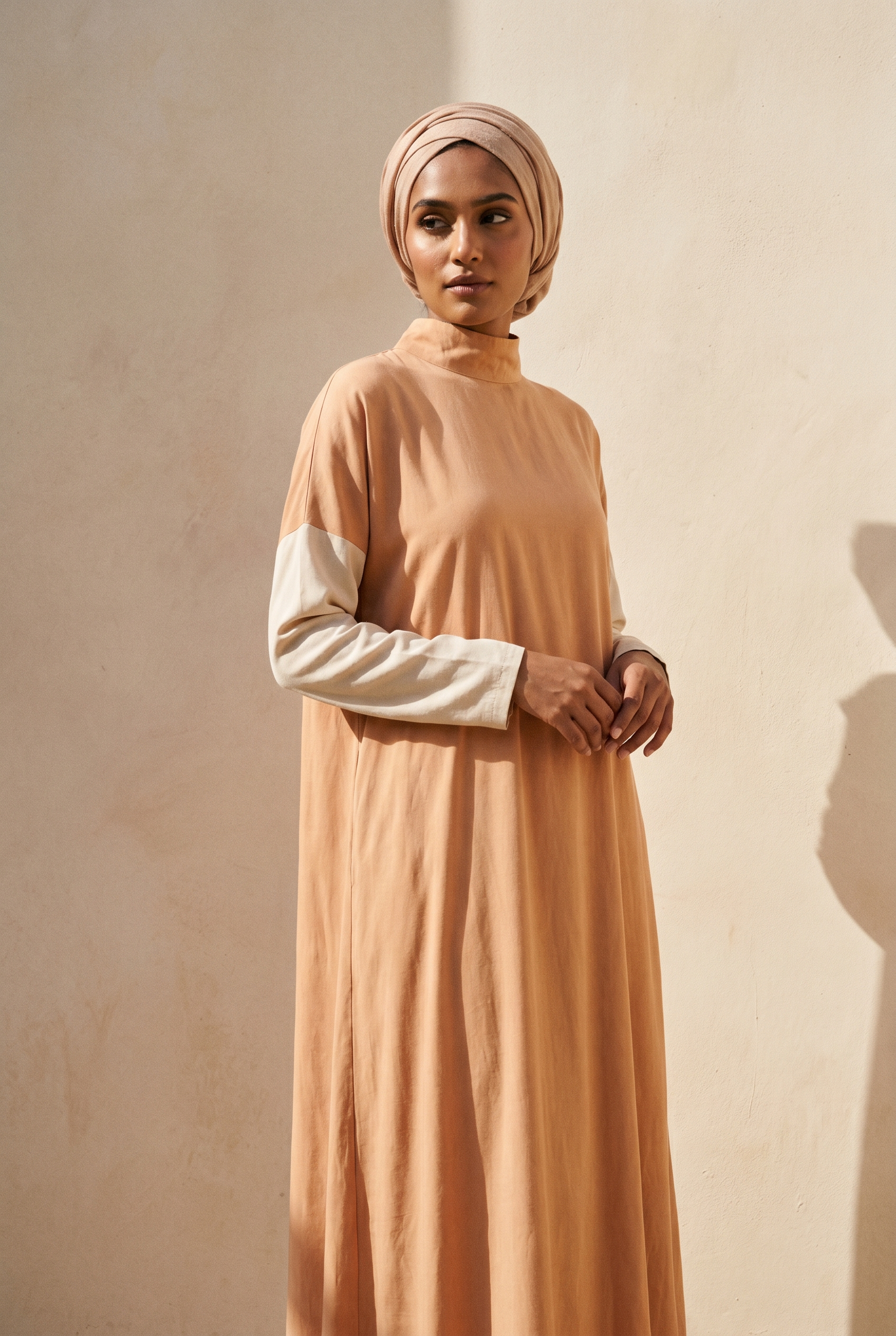 A model wears a modest full-length Aeshal dress in soft saffron and bone tones